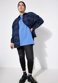 Camicia di flanella a quadri blu su una t-shirt blu, abbinata a jeans skinny neri con strappi e scarpe con plateau nere decorate con borchie.