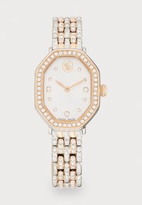 Montre octogonale avec un cadran blanc, lunette en or rose et bracelet en argent avec des accents en cristaux transparents. Fabriquée en Suisse, design épuré.