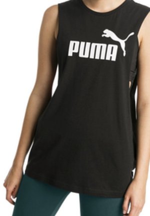 Henkilö pukeutuneena mustaan hihattomaan Puma-paitaan, jossa on valkoinen logo, yhdistettynä tummanvihreisiin housuihin, seisoo käsivarret rennosti sivuilla.