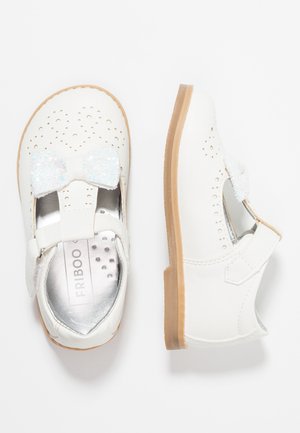 Hvide lædersko med perforerede detaljer og en glitrende hvid sløjfe. Har en velcrolukning og en lysebrun gummisål.