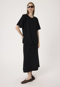 Sort oversized t-shirt og matchende midi-nederdel, begge lavet af glat stof. Båret med brune ballerinaer og mørke solbriller.
