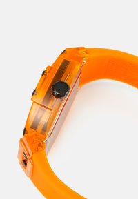 Digital klocka med ett transparent orange hölje och orange silikonrem. Har svarta knappar och en slät, blank yta.