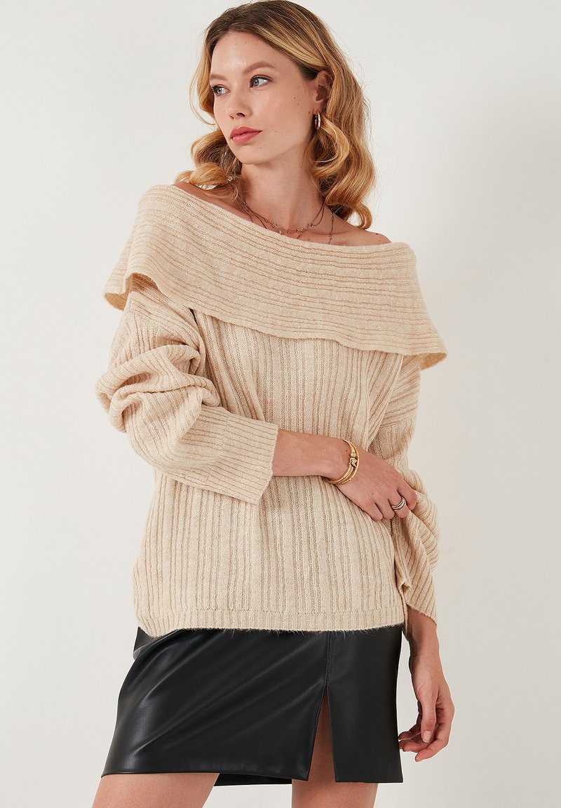 Hele beež off-the-shoulder kudum sweater, millel on ribikonstruktsioon, pikad varrukad ja lõdvestunud lõige. Kombineeritud musta nahast mini-seelikuga.