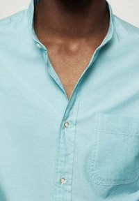 Hellblaues Baumwollhemd mit Knöpfen, ausgestattet mit einem Kragen und einer einzelnen Brusttasche. Glatte Textur mit einfarbigem Design.