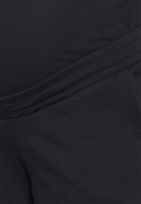 Tessuto di cotone nero che mostra una superficie liscia con cuciture sovrapposte, creando un effetto a strati. Nessun motivo o hardware visibile.
