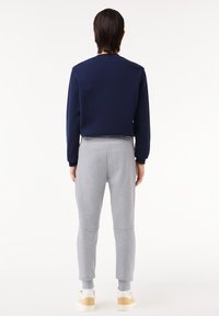 Hanorac cu guler rotund de culoare bleumarin, asortat cu pantaloni jogger tapered de culoare gri deschis, având talie elastică și tivuri cu manșete, purtat cu adidași albaștri și bej.