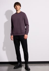 Sudadera de cuello redondo morada con puños y dobladillo acanalados, combinada con pantalones negros y botas negras hasta el tobillo. Diseño limpio sin marcas visibles.