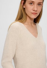 Beige gebreide trui met een V-hals, aansluitend ontwerp, geribbelde textuur, lange mouwen en subtiele naden.