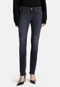 Ciemnoszare obcisłe dżinsy wykonane z denimu, z talią o średnim kroju, subtelnym przeszyciem i dopasowanym krojem, zestawione z czarnymi butami na wysokim obcasie.