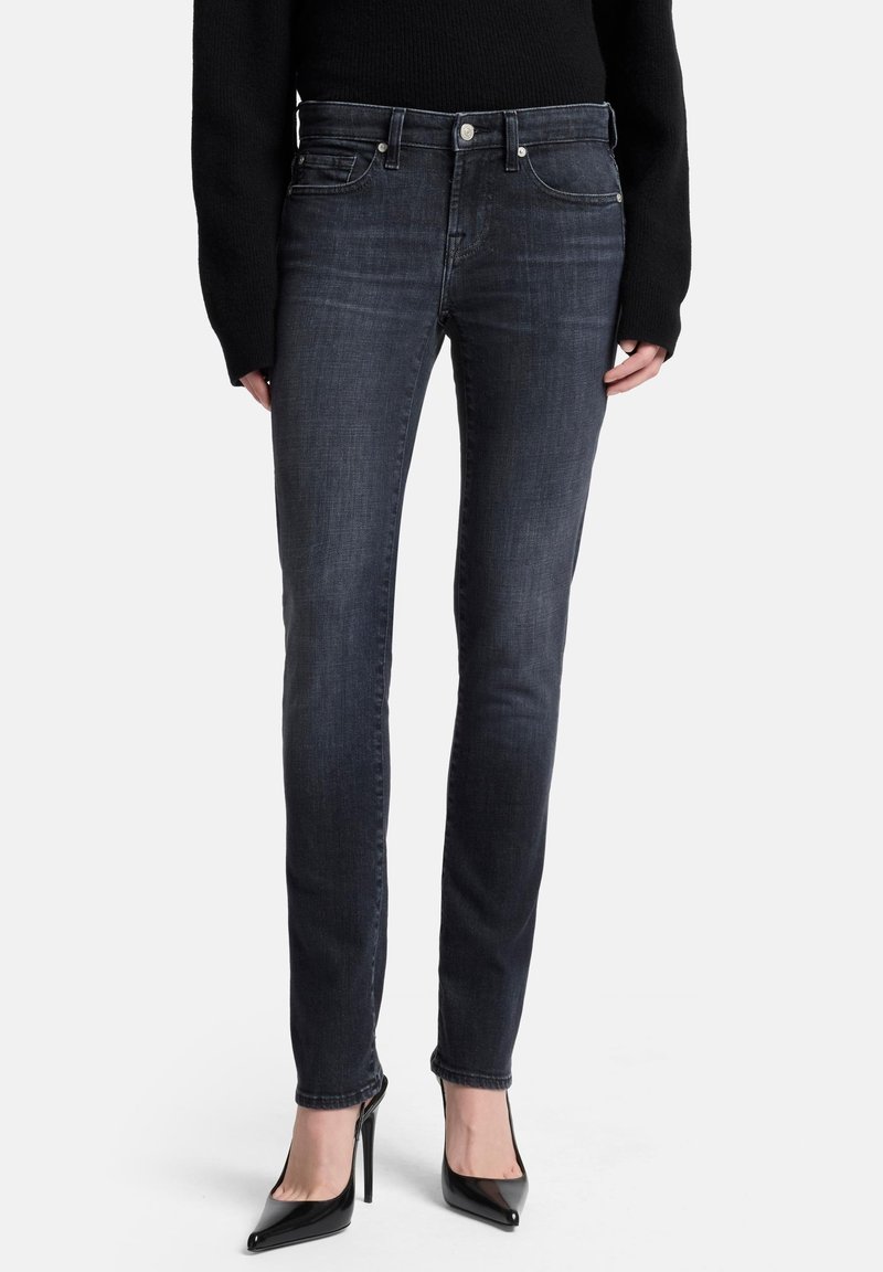 Ciemnoszare obcisłe dżinsy wykonane z denimu, z talią o średnim kroju, subtelnym przeszyciem i dopasowanym krojem, zestawione z czarnymi butami na wysokim obcasie.