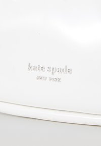 Biely kabelka s embosovaným logom "kate spade NEW YORK". Hladká textúra, zaoblený tvar, minimalistic design a žiadne viditeľné kovanie.