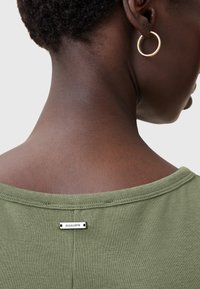 Suéter verde oliva con un escote amplio, que presenta una etiqueta metálica de la marca en la parte trasera. Tejido ligero y texturizado visible en el escote.