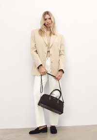 Blazer oversize beige, top crema, pantaloni bianchi. Borsa a tracolla in suede nera con dettagli in pelle e accessori in oro. Mocassini neri con finitura testurizzata.
