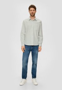 Ein Button-up-Hemd mit hellblauen und grünen vertikalen Streifen, kombiniert mit blauen Jeans und weißen Turnschuhen. Das Hemd hat eine Brusttasche.
