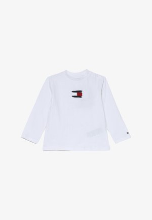 Camicia bianca a maniche lunghe con scollo rotondo, con un piccolo disegno astratto in nero, rosso e bianco sulla parte anteriore, e un dettaglio con bottoni sulla spalla.