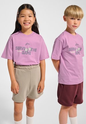 To børn iført matchende lavendelfarvede t-shirts med teksten "SERVE THE GAME". Den ene har beige shorts på; den anden har mørkerøde shorts.
