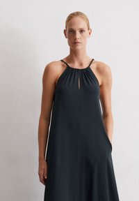 Dunkles, ärmelloses Kleid mit gerafftem Ausschnitt und einem Schlitz vorne. Hergestellt aus einem glatten Stoff mit einer lockeren, fließenden Silhouette.