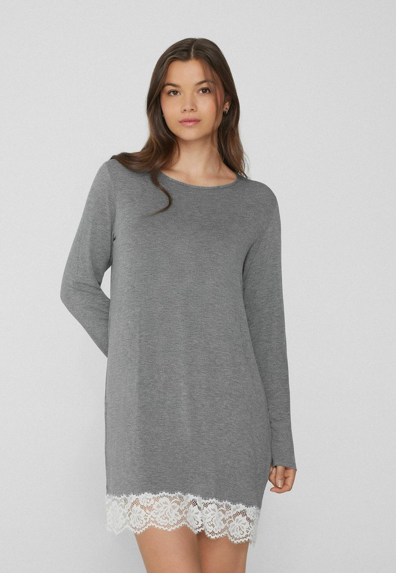 Vestido gris de manga larga con escote redondo y borde de encaje blanco en el dobladillo. Tejido suave con un corte holgado, que llega a medio muslo.