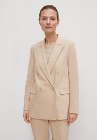 Beige Doppelreiher-Blazer aus glattem Stoff, ausgestattet mit Reverskragen, zwei Fronttaschen und vier Knöpfen auf der Vorderseite.