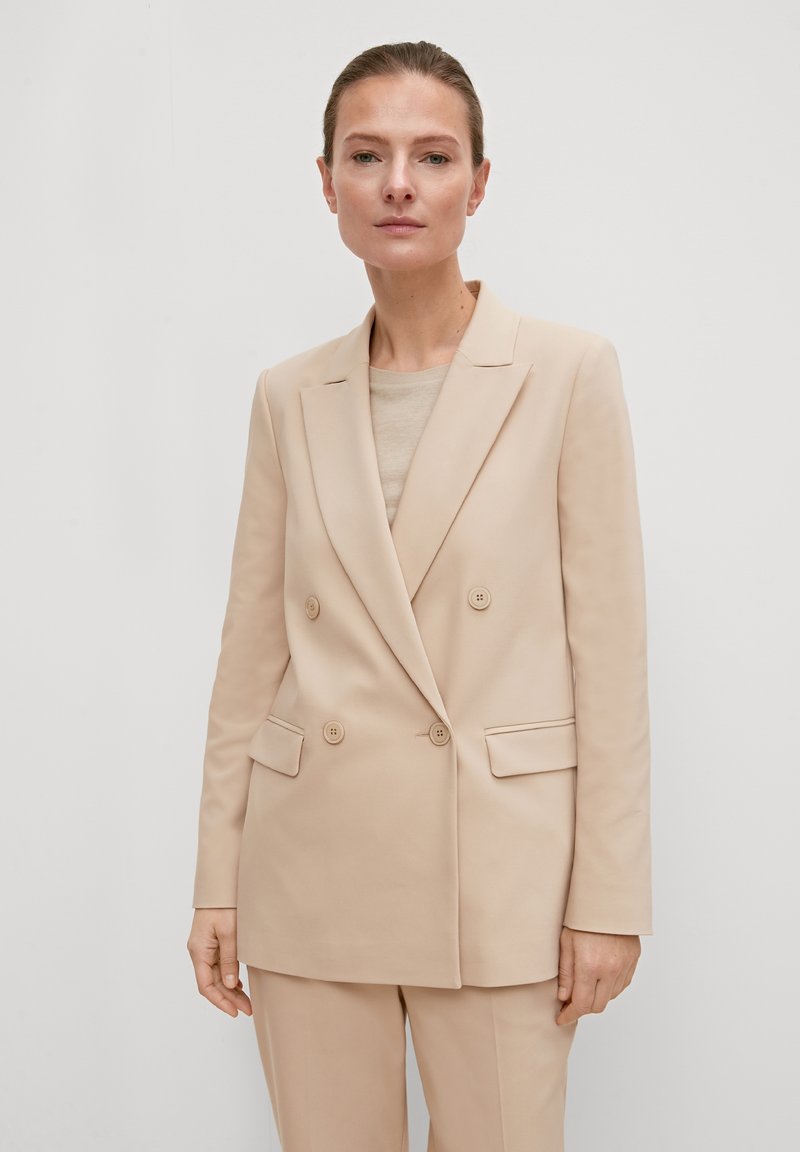 Blazer beige croisé en tissu lisse, avec des revers à cran, deux poches avant et quatre boutons sur le devant.
