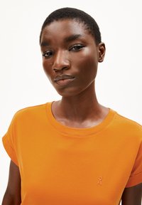 T-shirt orange à manches courtes retroussées et col rond. Présente un logo brodé subtil dans une teinte plus claire sur la poitrine.