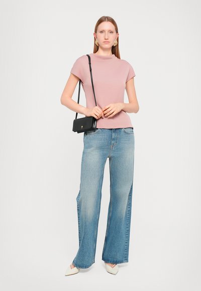 Light pink short-sleeve top paired with wide-leg light blue jeans and cream pointed-toe shoes. Black crossbody bag with gold accent detail.