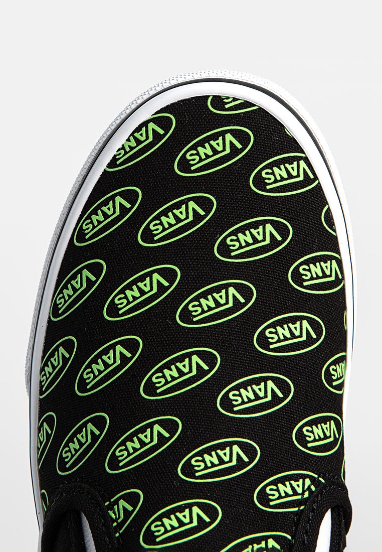 Schwarzer Canvas-Slip-On-Schuh mit einem sich wiederholenden grünen "VANS"-Logo-Muster, weißer Gummisohle und strukturiertem Obermaterial.