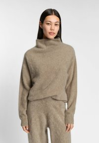 Beige ulltröja med hög, vikbar krage, avslappnad passform och långa ärmar, med en mjuk, fuzzy textur och ribbade muddarmar.