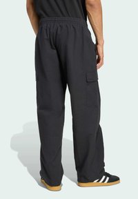 Pantalones cargo negros con cintura elástica, bolsillos laterales y corte holgado. La tela parece texturizada, adecuada para un estilo casual.