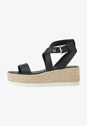 Sandalia de cuña de cuero negro con correas cruzadas en el tobillo, hebilla dorada, plataforma de yute trenzado y suela de goma blanca.