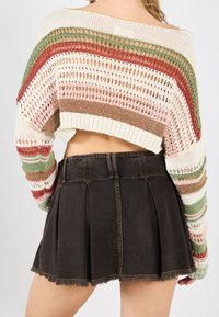 Pull en maille crochet avec rayures multicolores (rose, vert, rouge) associé à une jupe en jean foncé avec un design plissé et un ourlet effiloché.