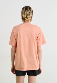 Short-sleeved, peach-colored t-shirt made of cotton. Loose fit with a crew neck and straight hem. Simple design, no patterns or accents.