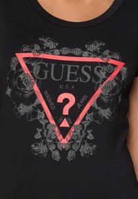 Svart T-shirt med en framträdande rosa triangellogo, blomsterdesignsinslag och texten "GUESS USA" samt "WASHED JEANS" i grått.