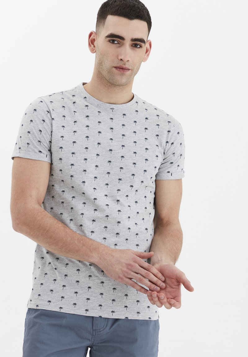 Grå bomulds t-shirt med korte ærmer, prydet med et gentaget sort palmetræsmønster. Enkel rund halsudskæring, let figursyet design.