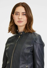 Giacca in pelle nera dal design aderente, con colletto alto, chiusura con zip, dettagli a coste sulle spalle e due tasche frontali con zip.