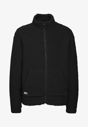 Giacca in pile nera con colletto alto, chiusura a cerniera completa, due tasche frontali e superficie morbida e testurizzata. Presenta un piccolo etichetta del marchio.