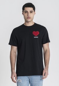 Černé bavlněné tričko s grafickým motivem červeného srdce a výšivkou "Kavanagh" na levé části hrudi. Krátké rukávy a design s kulatým výstřihem.