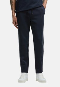 Navy sweatpants in a soft fabric with a straight cut, featuring front seam detailing and a drawstring waistband, paired with white sneakers.