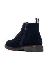 Botas de ante azul marino hasta el tobillo con cremallera lateral, punta redonda y suela de goma plana con banda de rodadura elevada para mayor tracción. Detalle de tira de dos tonos.
