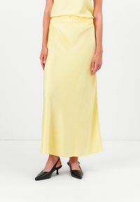 Gul sateng maxi-skjørt med elastisk midje, glatt tekstur og en flytende design; satt sammen med svarte spisse hæler.