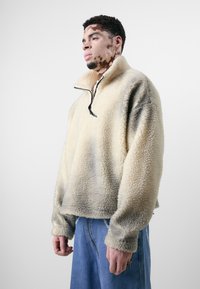 Fleece-Pullover in Creme mit einem Viertelreißverschluss und schwarzen Akzenten. Verfügt über eine strukturierte, flauschige Oberfläche und eine übergroße Passform mit abfallenden Schultern.