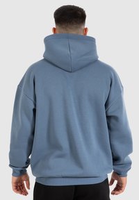 Felpa oversize blu chiaro con un ampio cappuccio, spalle scese e polsini e orlo a coste. Il tessuto sembra morbido con una texture liscia.