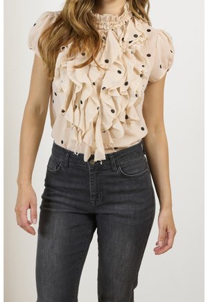 Lichtroze blouse met ruches en zwarte polka dots, voorzien van een hoge hals en korte pofmouwen, gecombineerd met donkere denim jeans.