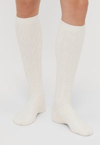 Knee-high cream socks made of textured knit material featuring a diamond pattern, ribbed cuff, and smooth toe area.