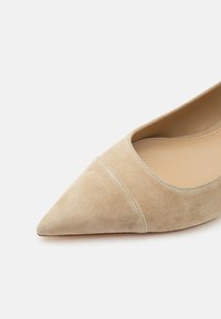 Chaussure plate en daim beige à bout pointu, avec une couture simple et une doublure intérieure en cuir lisse couleur fauve.