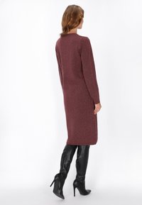 Rochie tricotată burgundă cu mâneci lungi, finisaj texturat și accente cu nasturi pe laterale. Asortată cu cizme negre de înălțime până la genunchi.