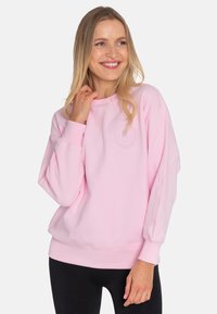 Light pink sweatshirt with a round neckline and long, slightly ballooned sleeves. Features a subtle logo on the chest and a ribbed hem.
