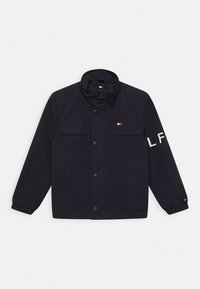 Marineblaues Jacket aus synthetischem Material mit hohem Kragen, vorderen Knöpfen, zwei Seitentaschen und einem gestickten Logo am Ärmel.