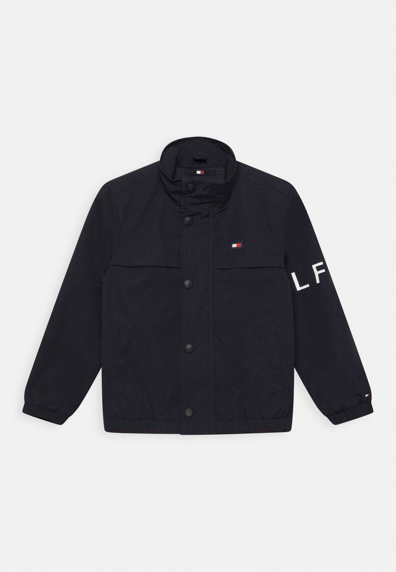 Marineblaues Jacket aus synthetischem Material mit hohem Kragen, vorderen Knöpfen, zwei Seitentaschen und einem gestickten Logo am Ärmel.