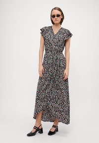 Robe maxi florale avec un fond noir, manches courtes à volants et ceinture à nouer. Présente une fente sur le côté et des motifs de fleurs multicolores.